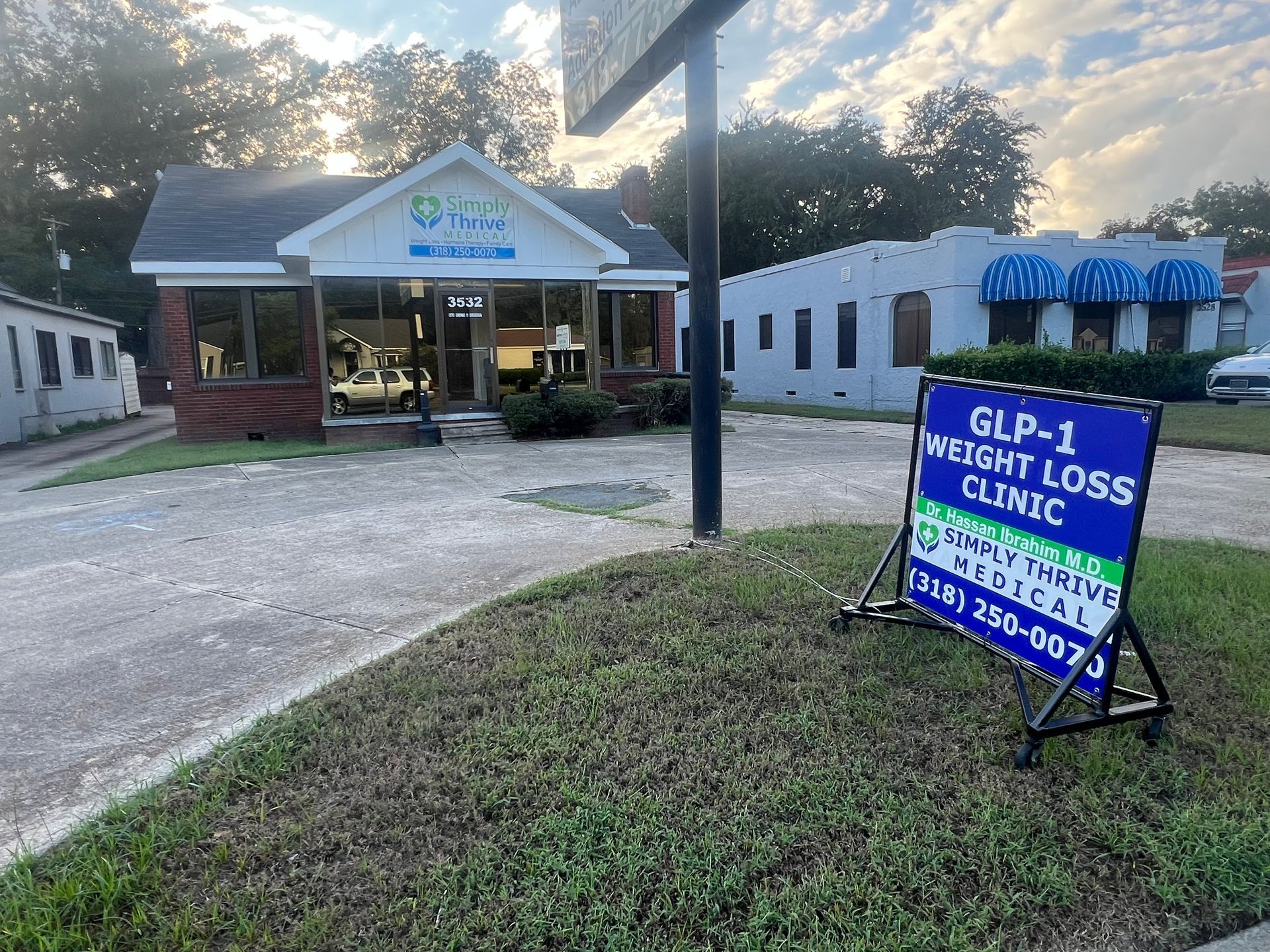 A small clinic with a sign for a GLP-1 weight loss clinic, green and blue colors, outdoors.