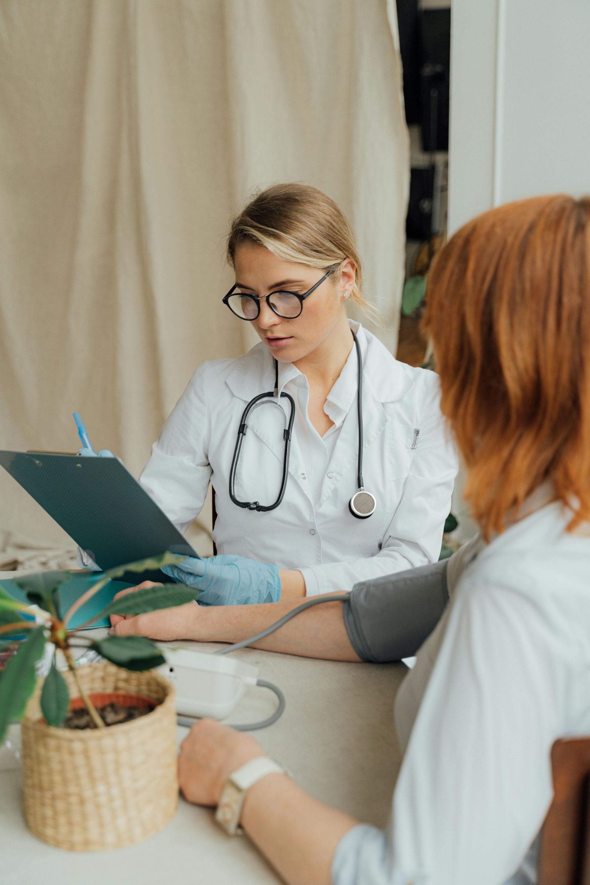 Doctor takes patient's blood pressure, recording notes. Setting appears to be a medical office.