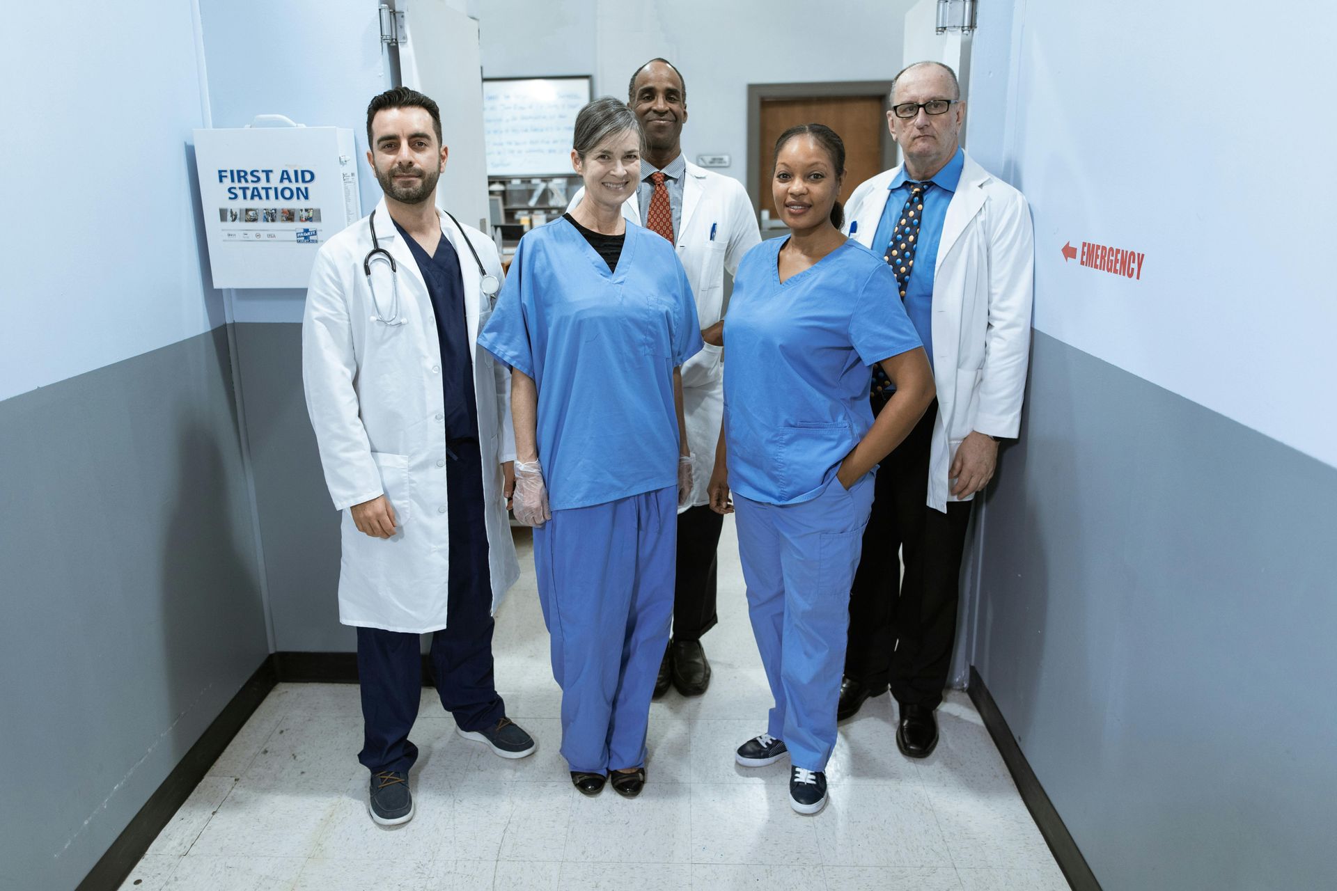 Medical team in scrubs and lab coats standing in a hallway near a first aid box.