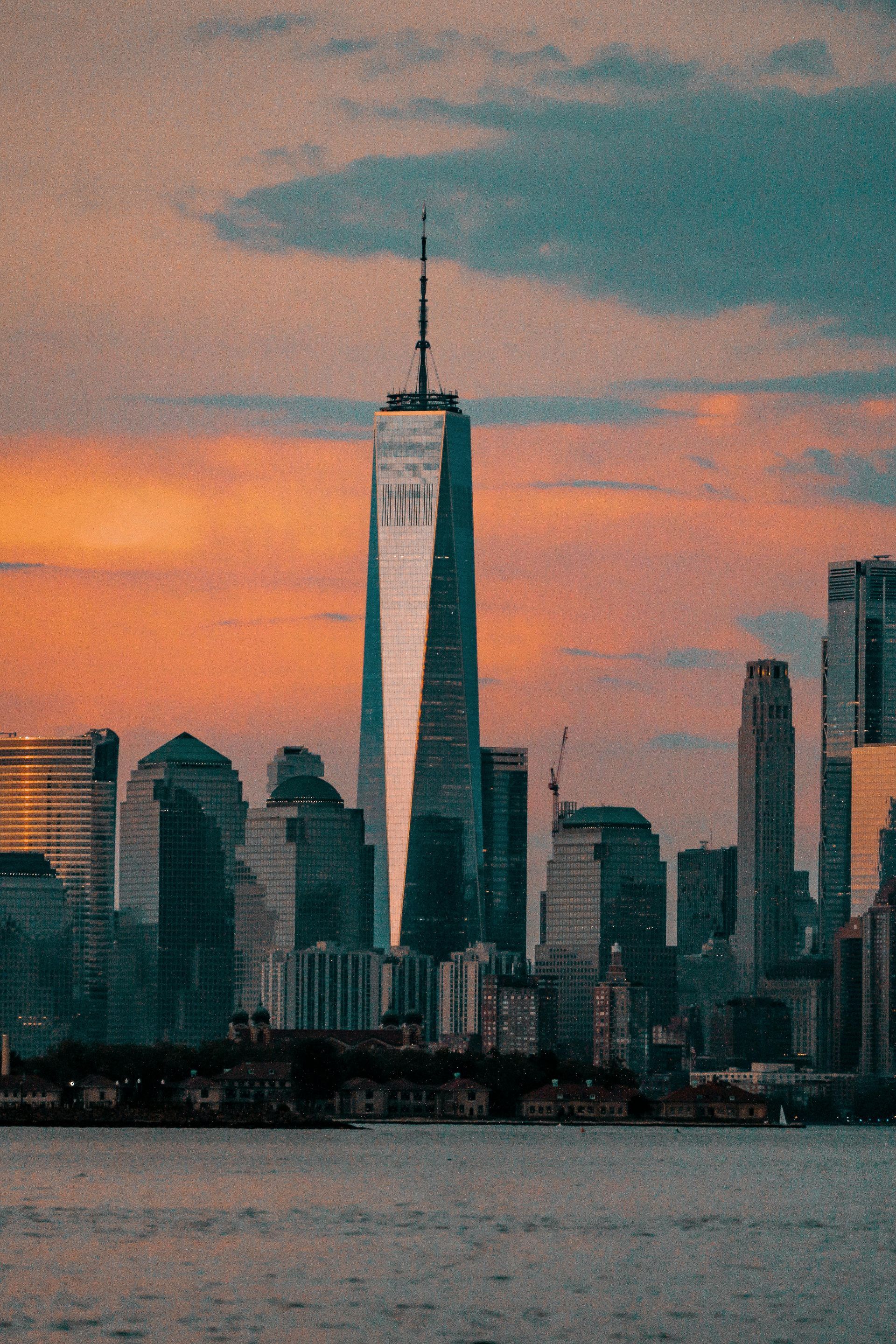 Sunset skyline with One World Trade Center above water and silhouetted buildings