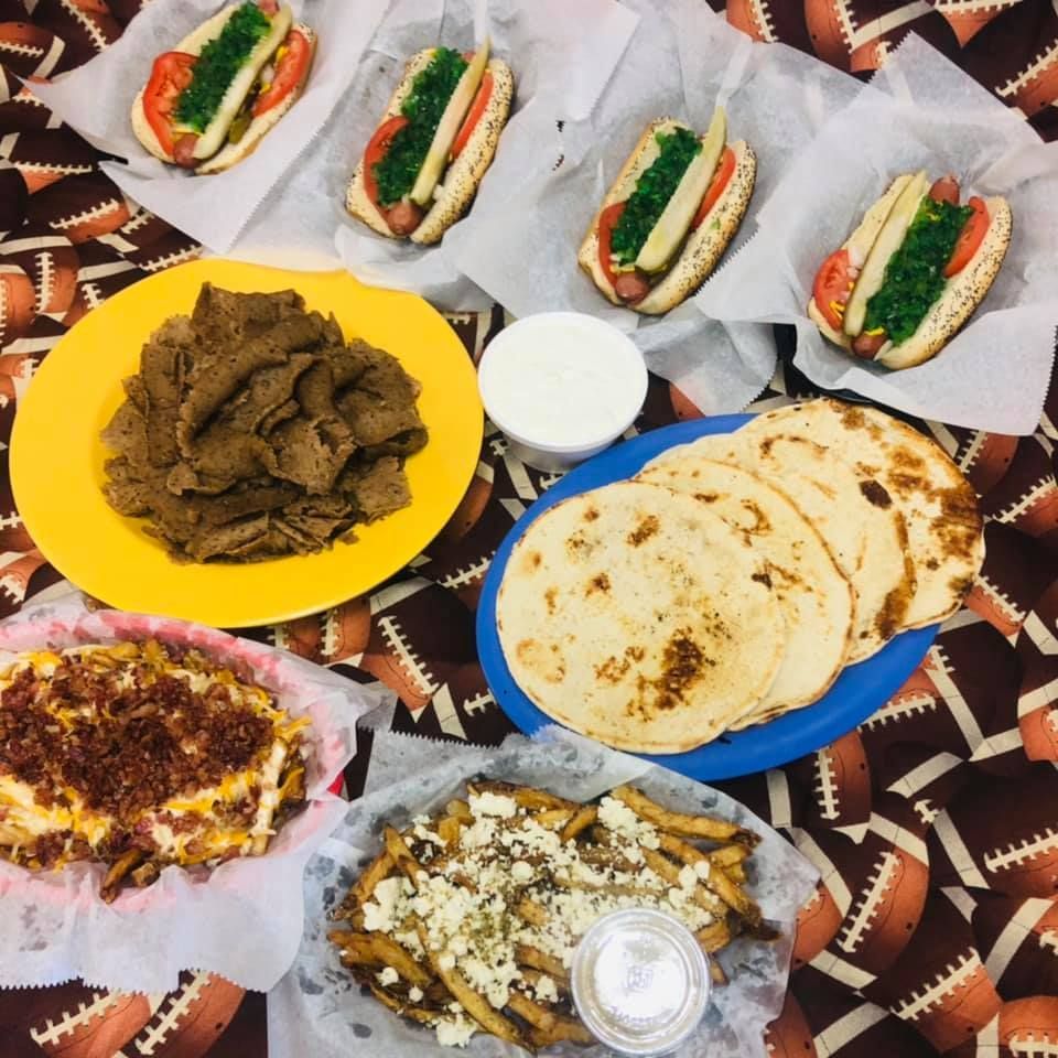 Assorted dishes on a patterned cloth, including flatbread, wraps, stew, rice, and dips arranged for a meal