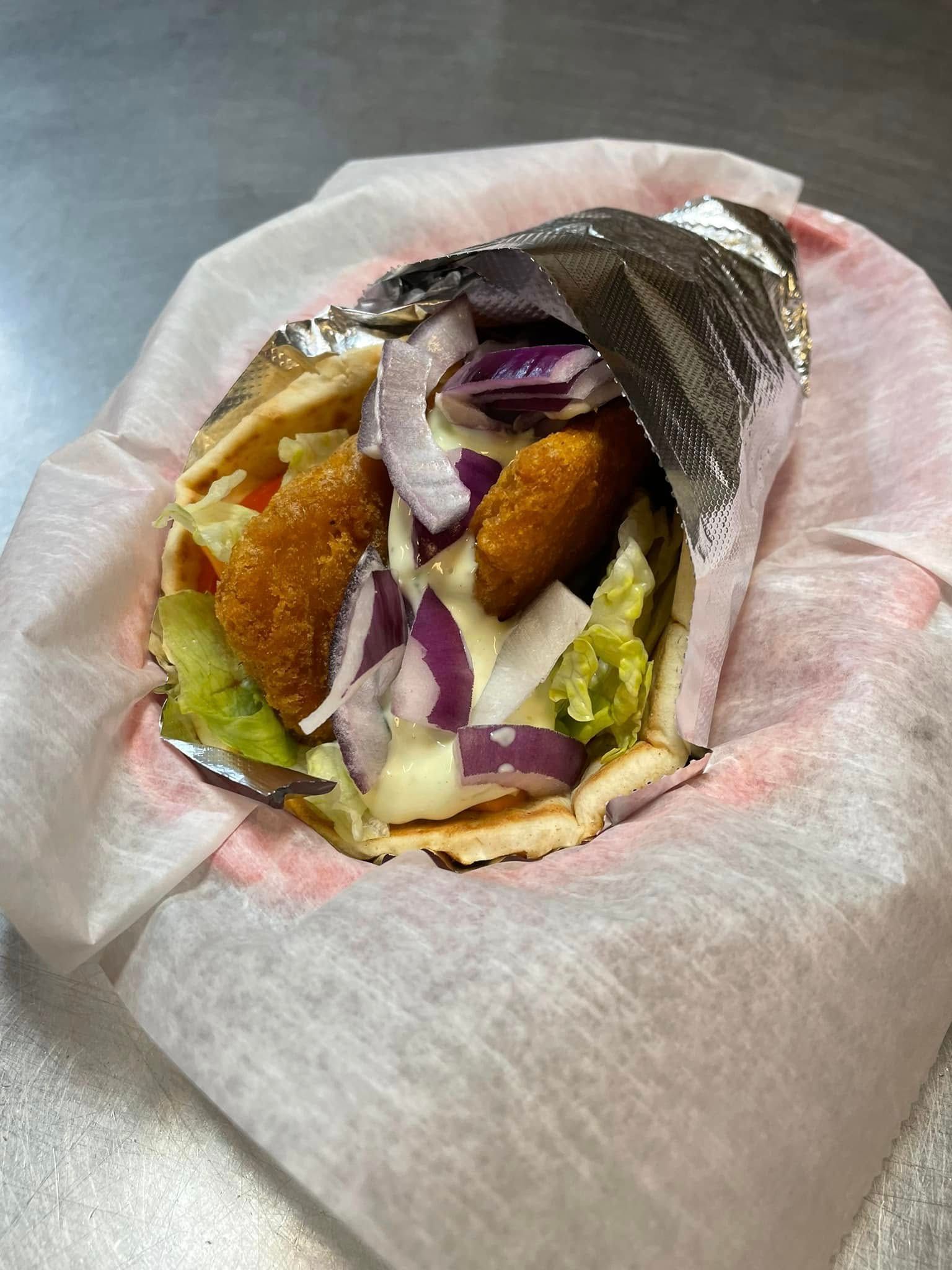 Partially eaten wrap with purple cabbage, lettuce, and fried filling in a paper wrapper on a table