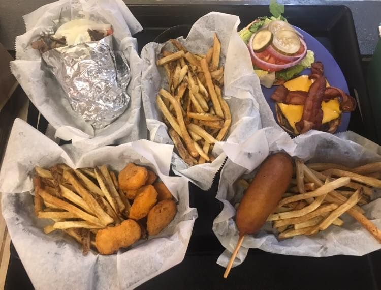 Assorted fast food trays with fries, burgers, hot dog, and fried appetizers on a table