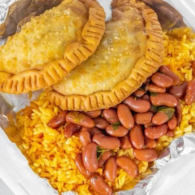 Two fried empanadas on yellow rice topped with red beans in foil container