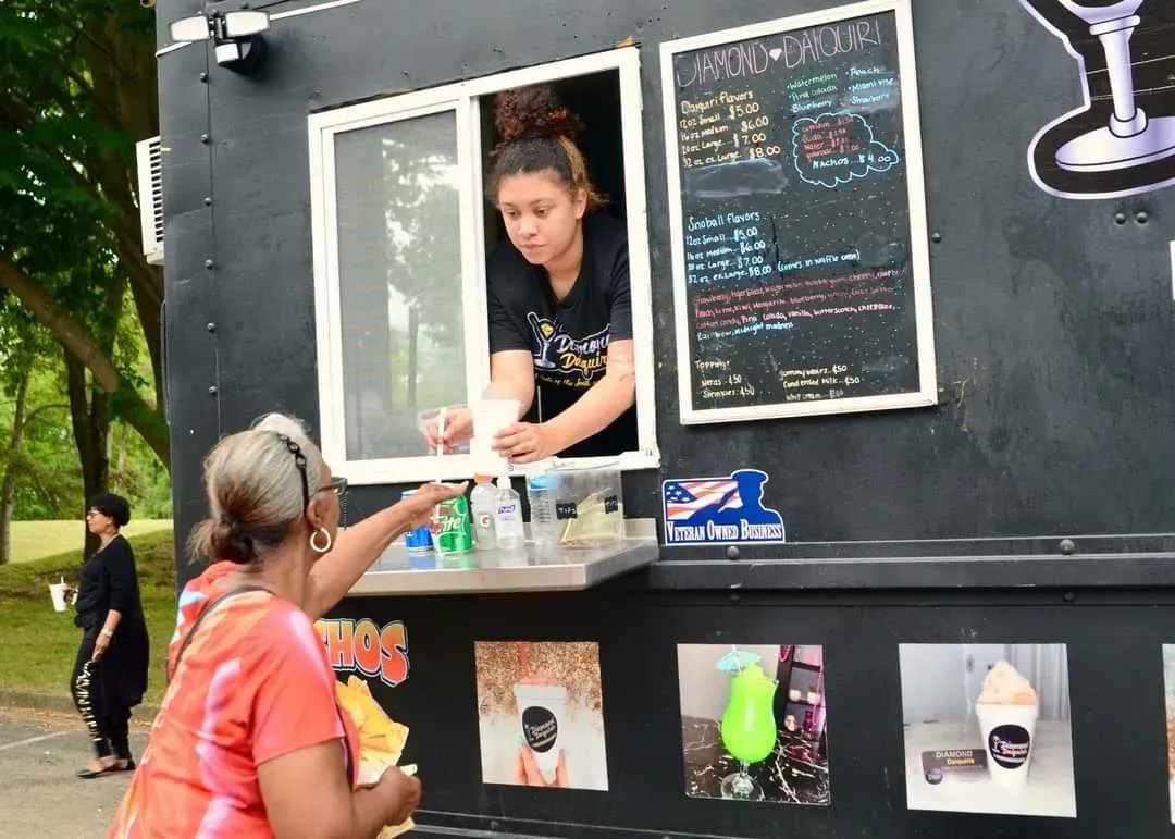Woman orders from a food truck window as the vendor hands over a drink.