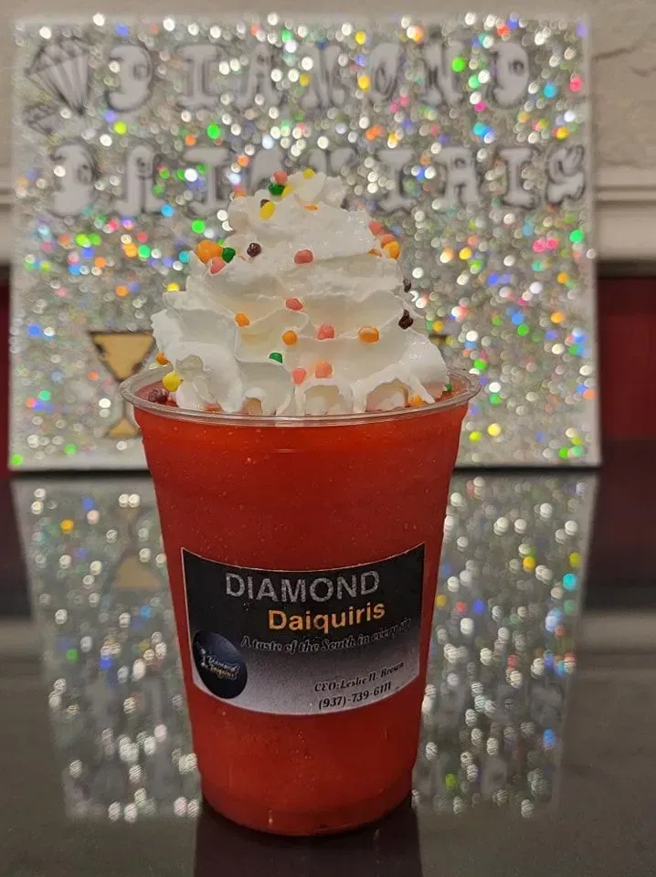 Red daiquiri drink in a clear cup with whipped cream and sprinkles, against a sparkly silver backdrop