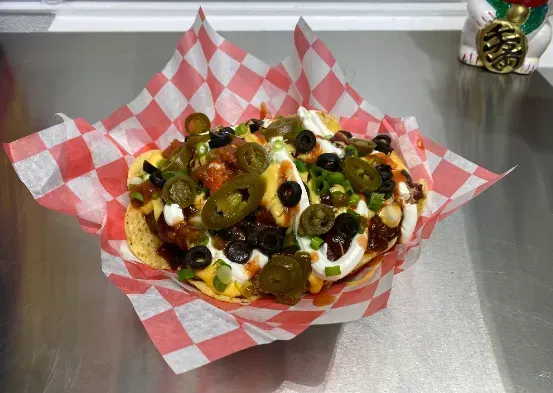 Loaded nachos topped with jalapeños, olives, cheese, and sour cream on red checkered paper.