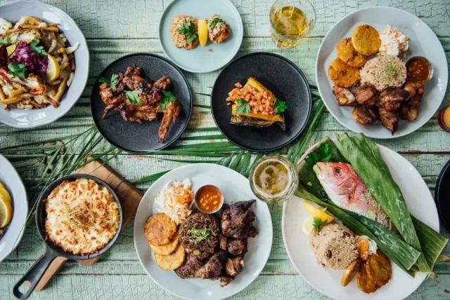 Assorted plated gourmet dishes on a light blue table, including salads, rice, seafood, and grilled meats.
