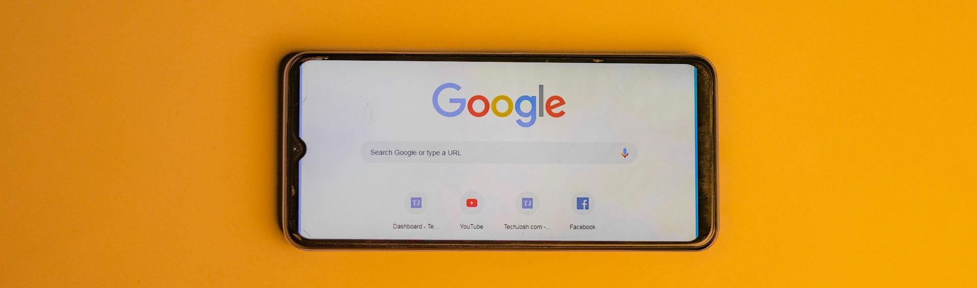 A cell phone is displaying the google search page on a yellow background.