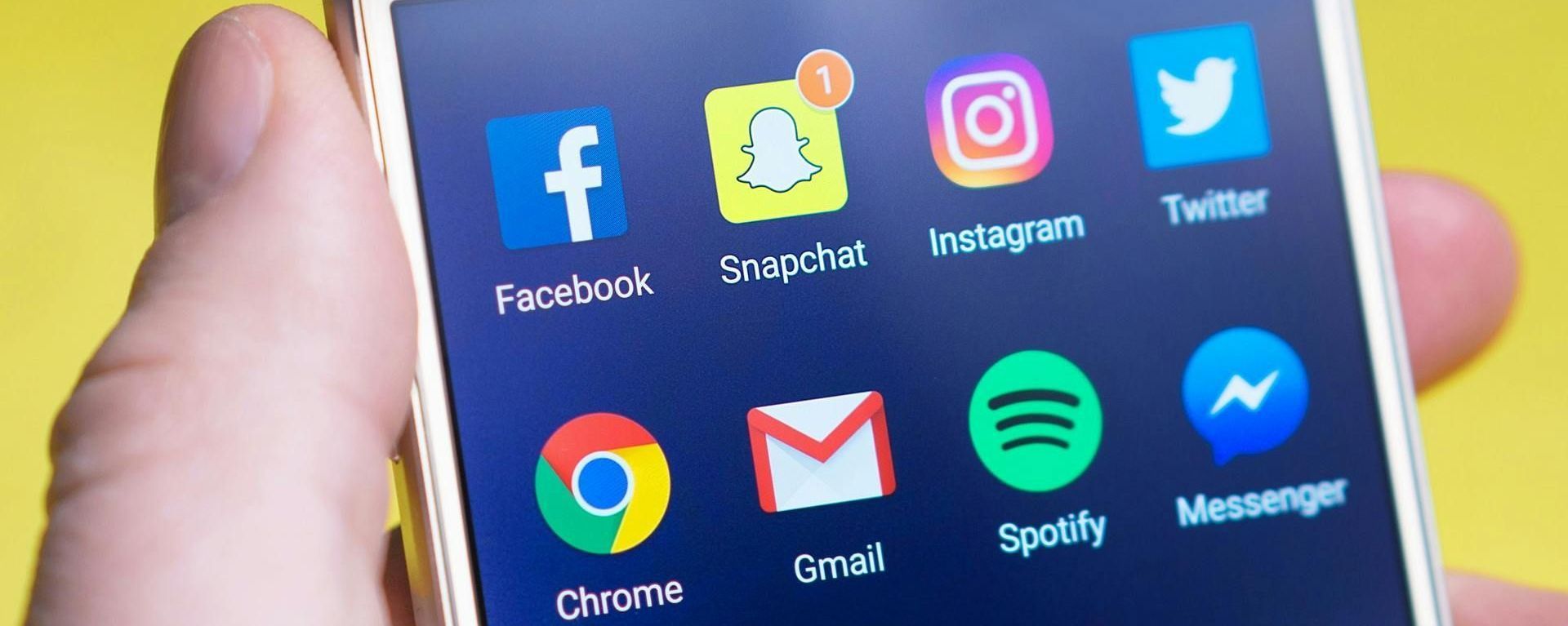 A person is holding a cell phone with social media icons on the screen.