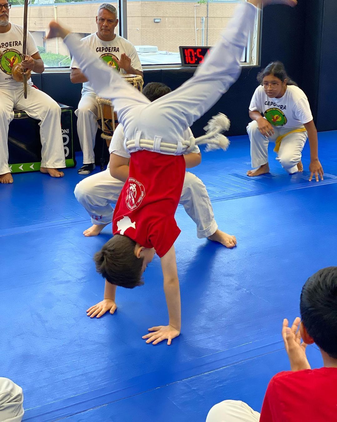 a boy in a red shirt is doing a handstand on a blue mat