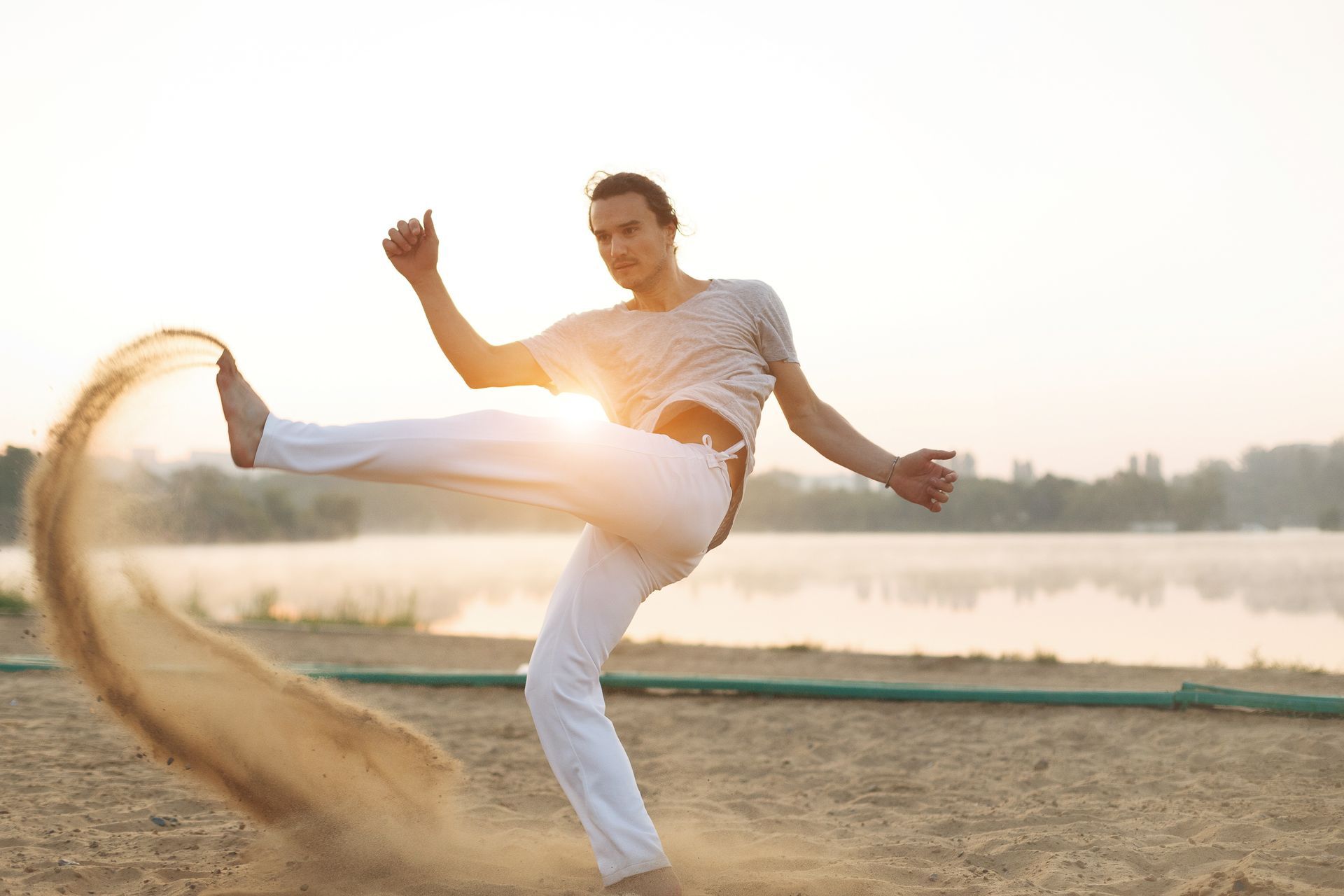 a man in white pants is kicking sand on a beach .