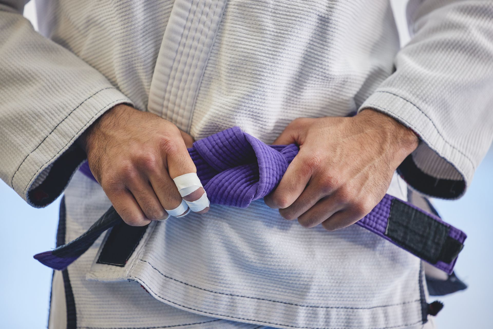 a man in a karate uniform is tying his purple belt .
