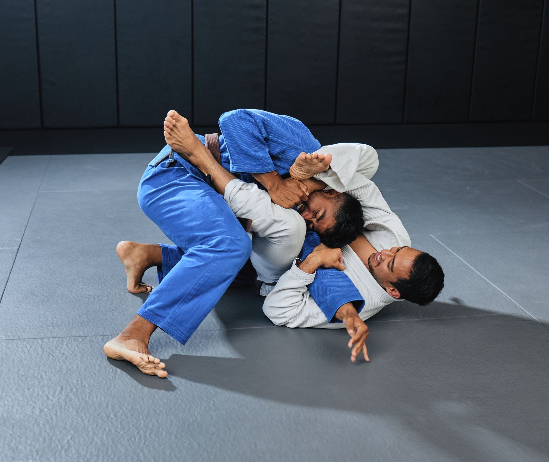 two men in blue and white kimonos are wrestling on a mat