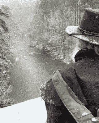 A black and white photo of a man in a hat looking at a river.