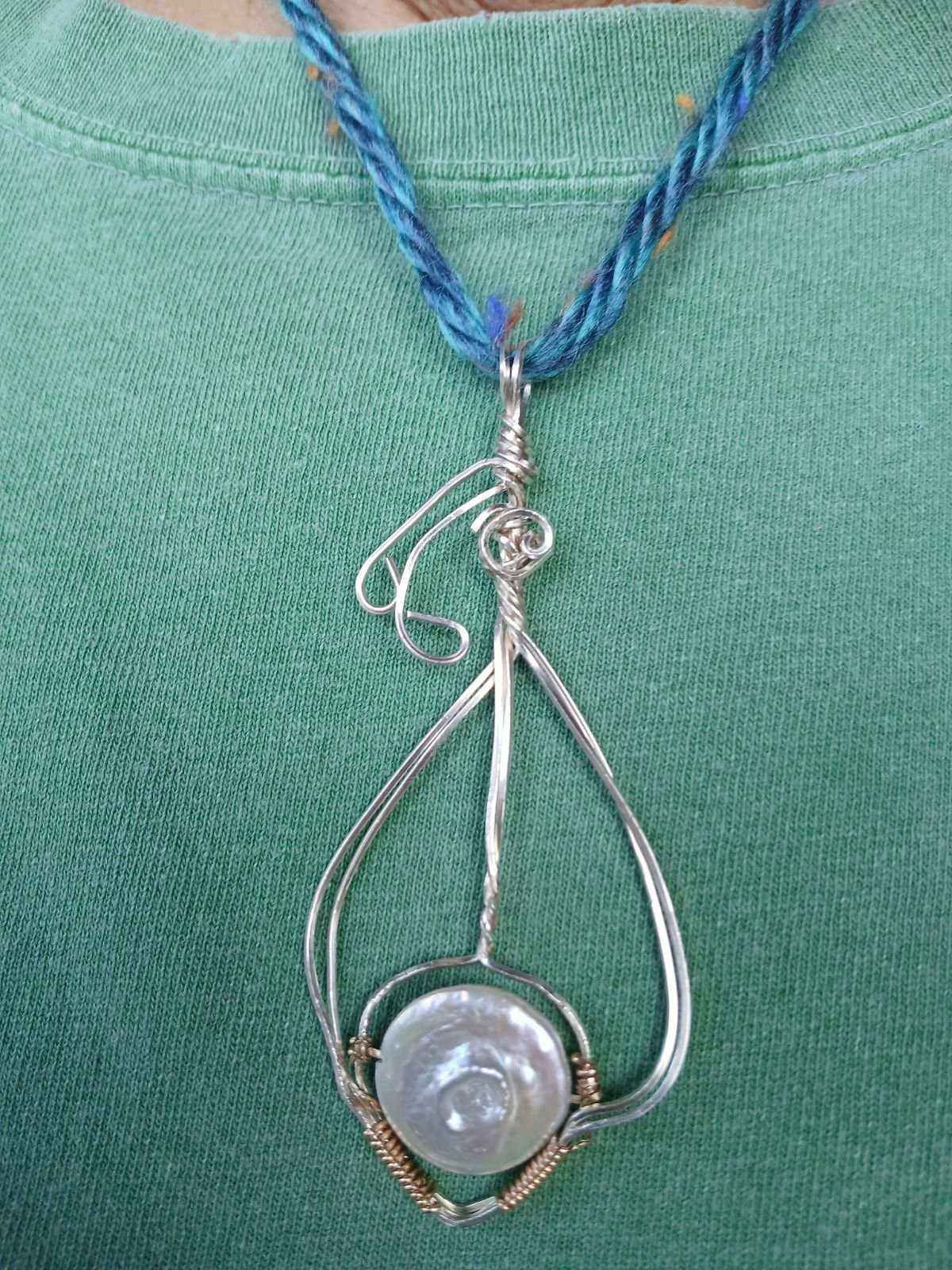 A close up of a person wearing a wire wrapped necklace with a pearl.