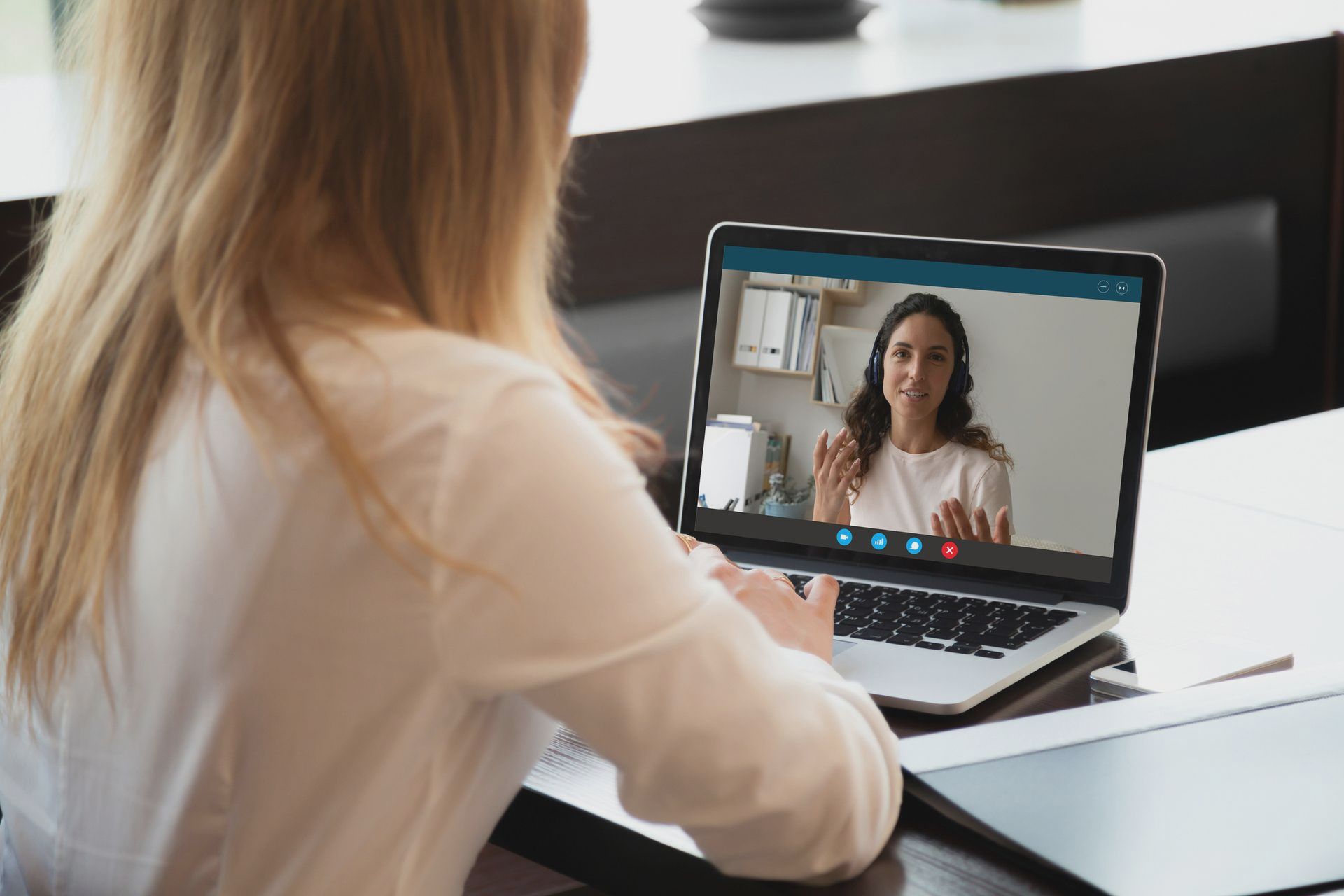 A woman is sitting at a desk using a laptop computer to have a video call with another woman.