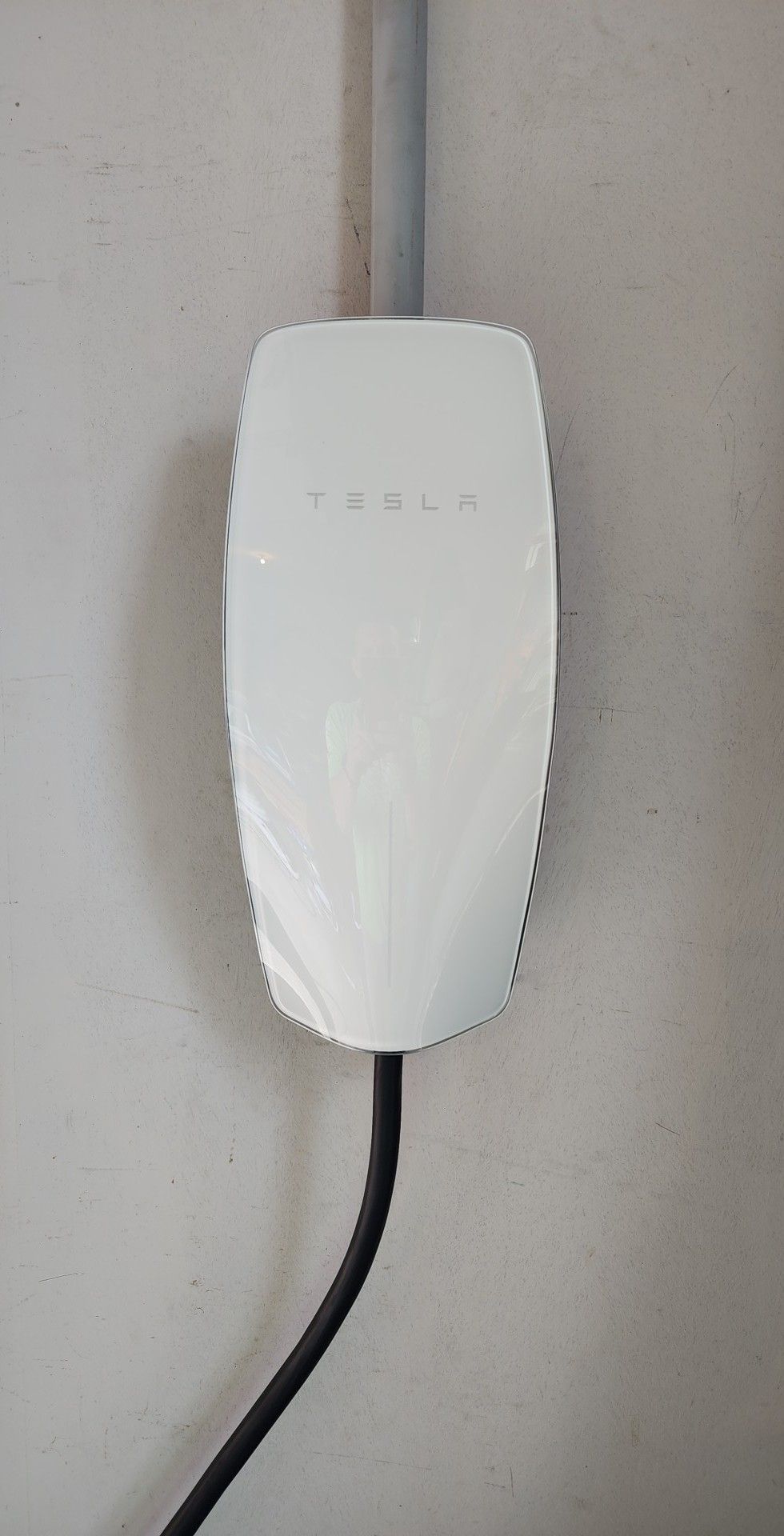 A white tesla charging station is attached to a wall.