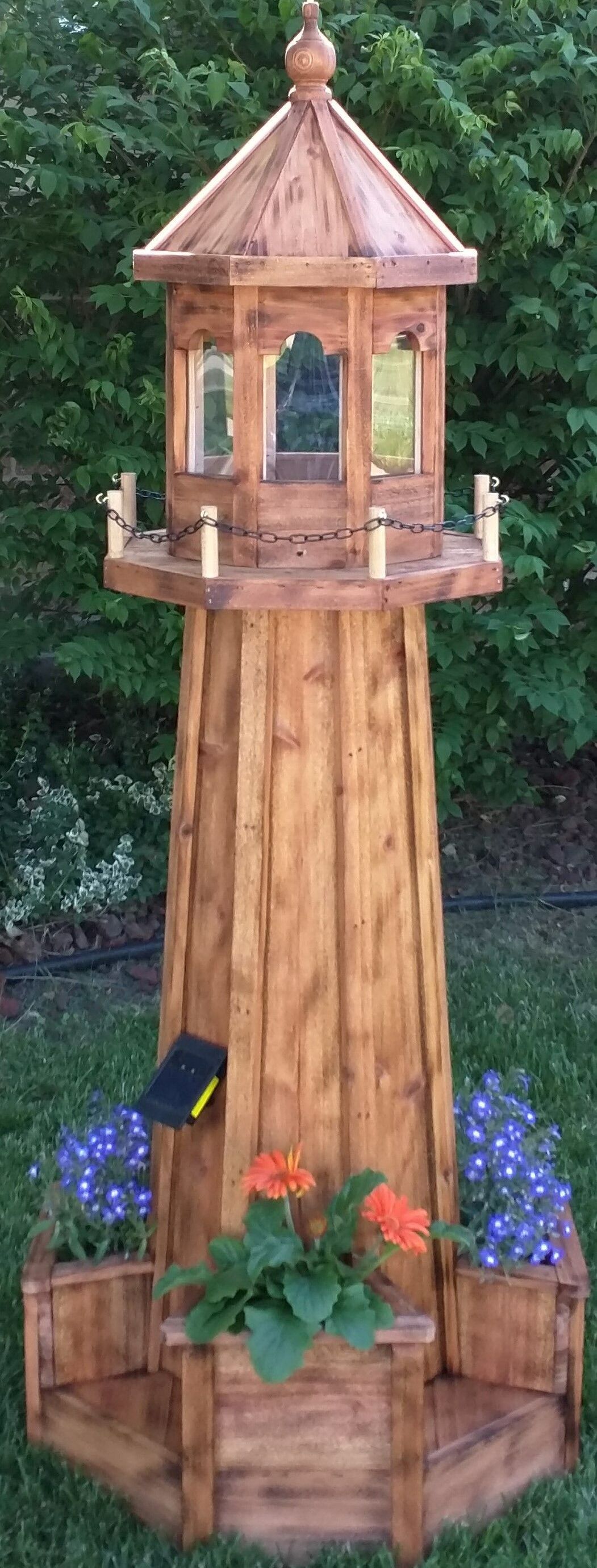 A wooden lighthouse planter with flowers in it is sitting on top of a lush green field.