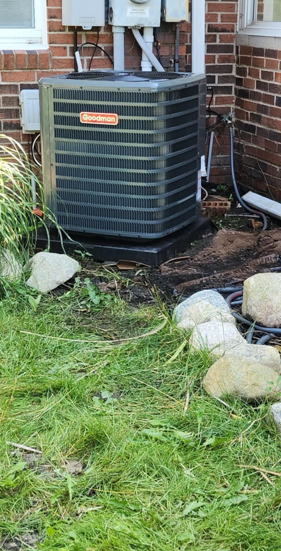 A black air conditioner is sitting in the grass next to a brick building.