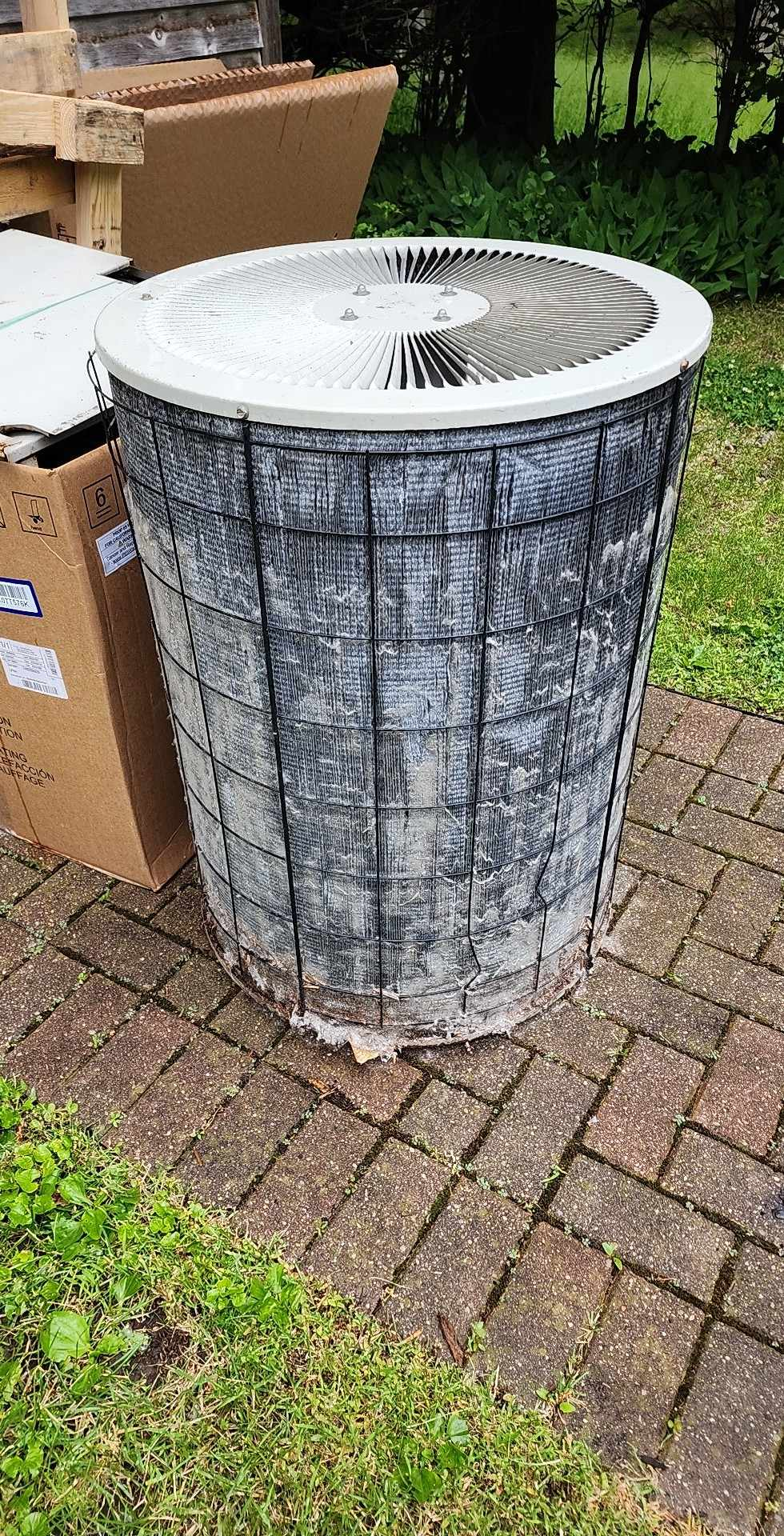 A large bucket is sitting on a brick sidewalk next to a cardboard box.