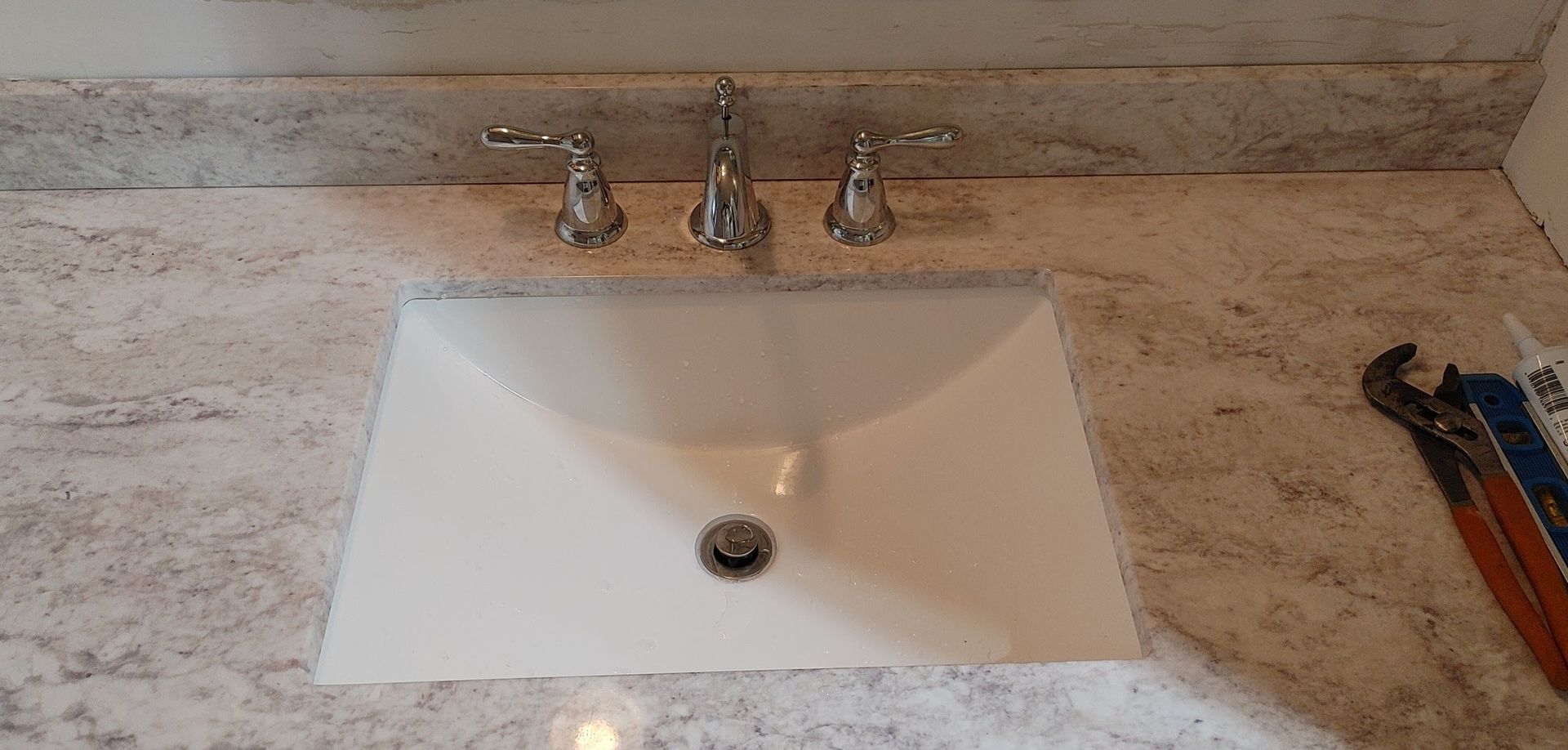 A bathroom sink is sitting on top of a granite counter next to a wrench.