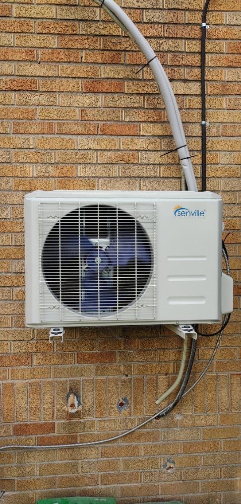 A white air conditioner is mounted on a brick wall.