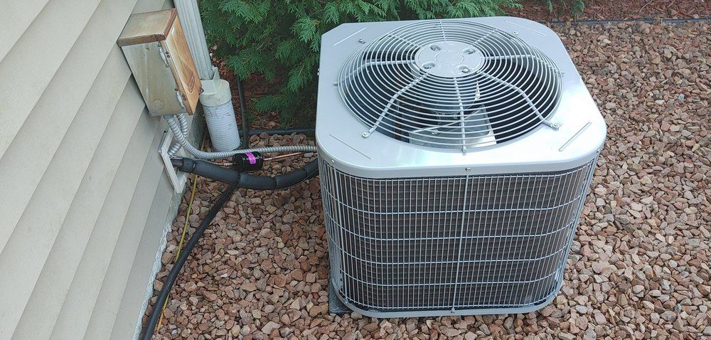 An air conditioner is sitting on a pile of gravel next to a house.