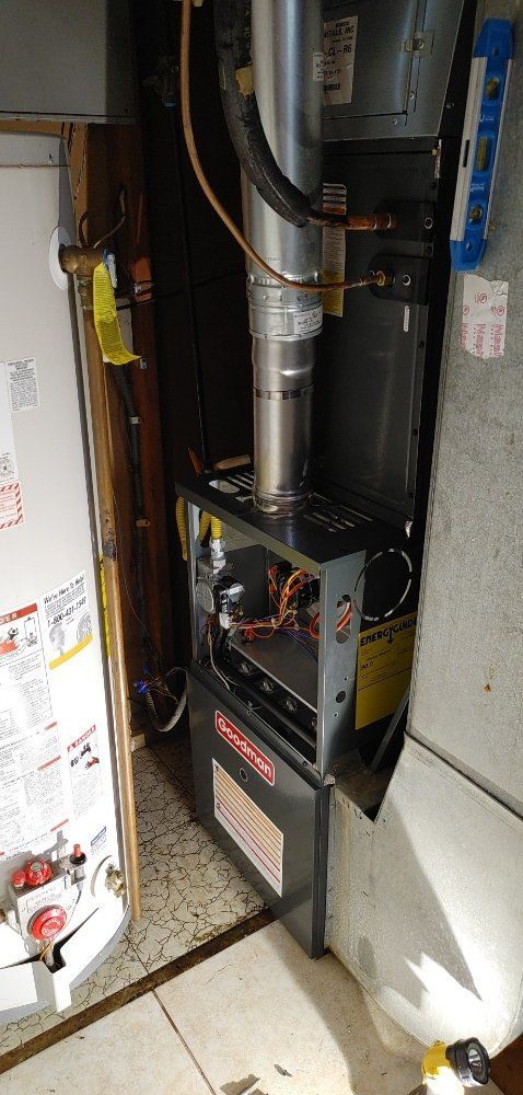 A furnace is sitting in a room next to a water heater.