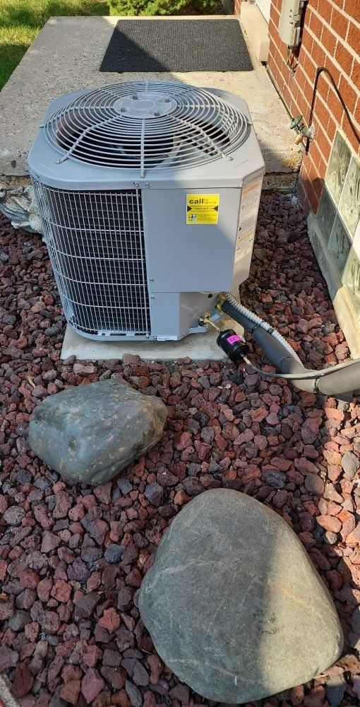 An air conditioner is sitting on top of a pile of gravel next to a brick building.
