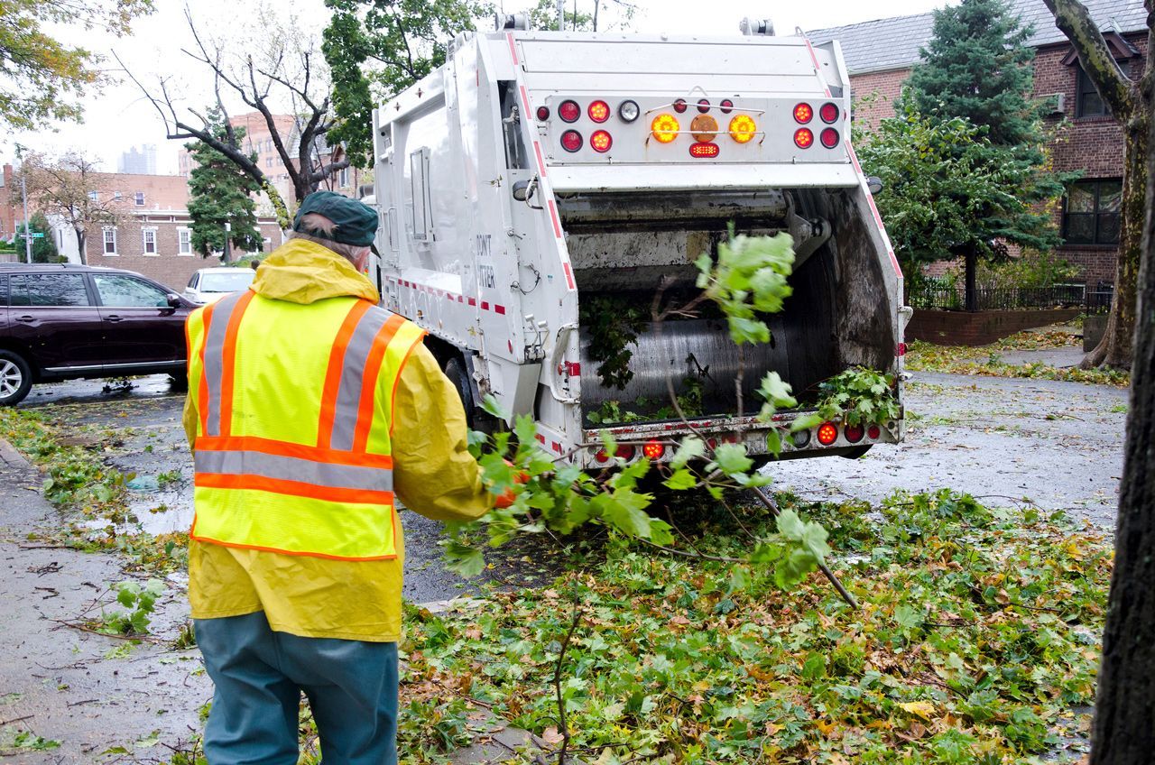 A man in a yellow vest is standing in front of a garbage truck.