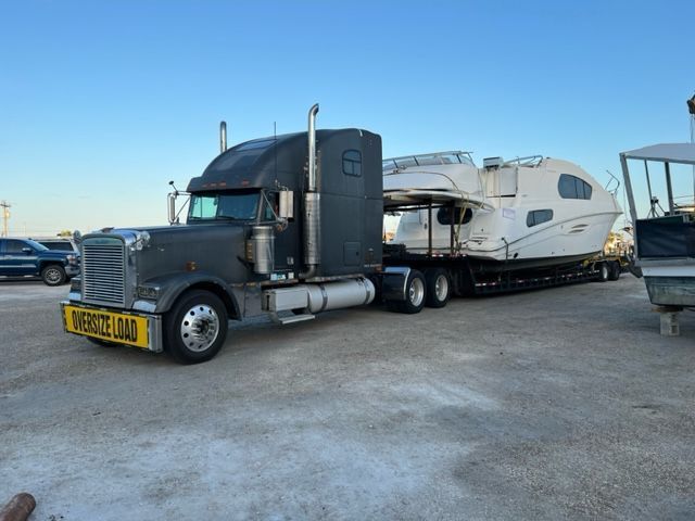 Semi-truck transporting a large white boat on a trailer. 
