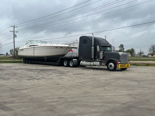 A semi-truck hauling a large white boat on a flatbed trailer.