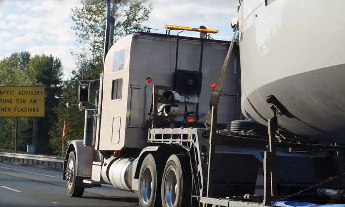A large semi-truck hauls a large, round object on a highway with a yellow road sign.