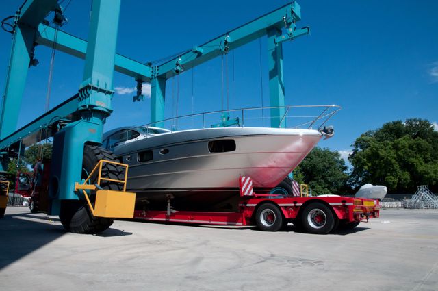 A large boat being lifted by a blue crane onto a red trailer on a sunny day.