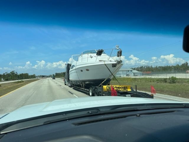 Boat being transported on a flatbed truck on a highway under a blue sky.