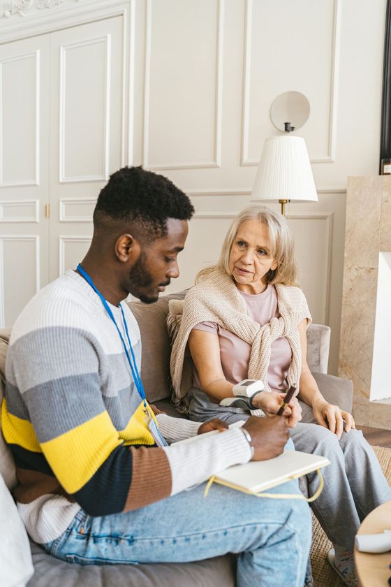 A man is sitting on a couch talking to an elderly woman.