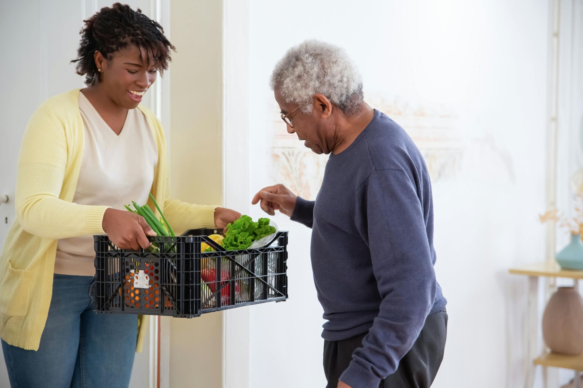 A woman is giving an elderly man a basket of vegetables.