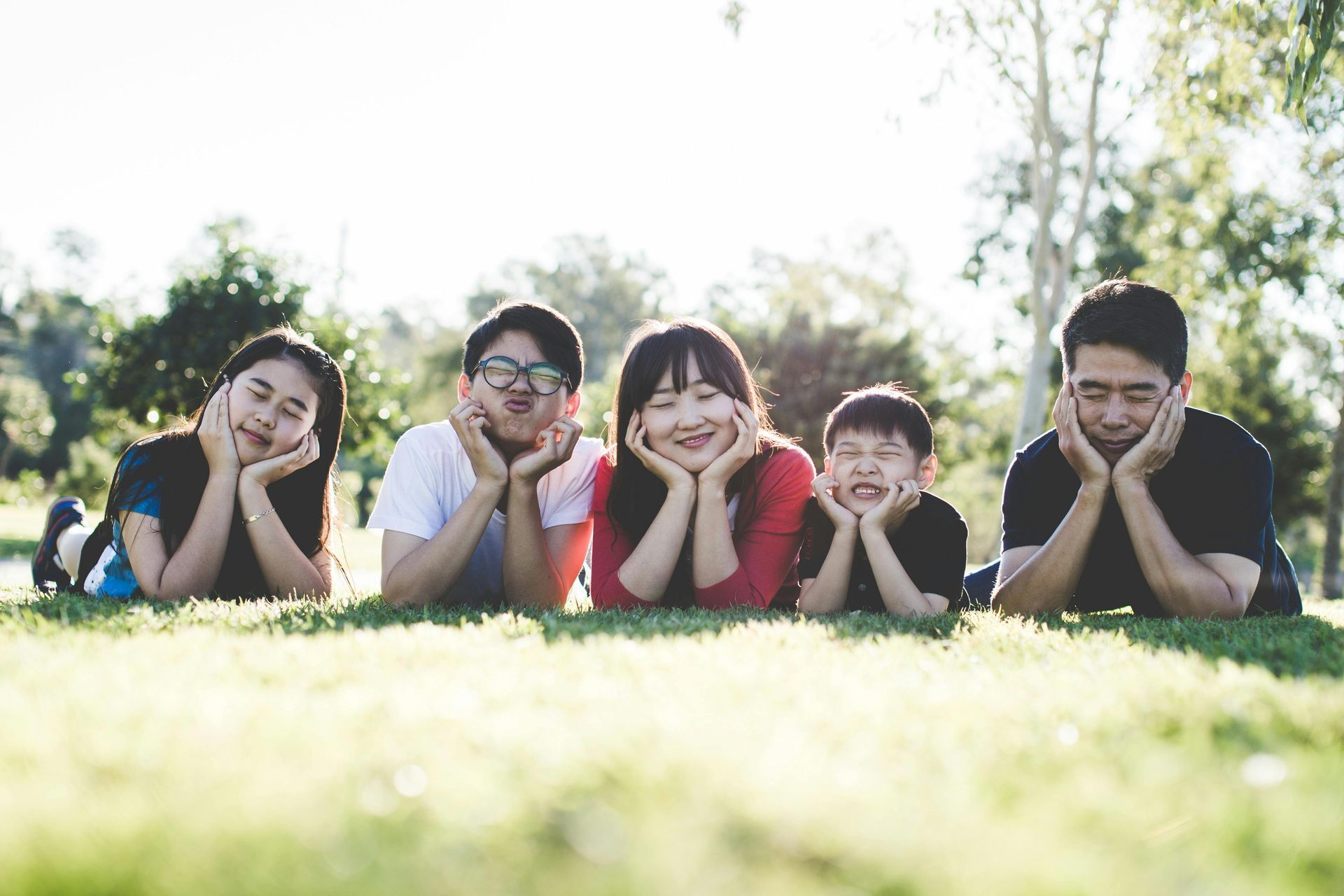 A group of people are laying in the grass with their hands on their faces.