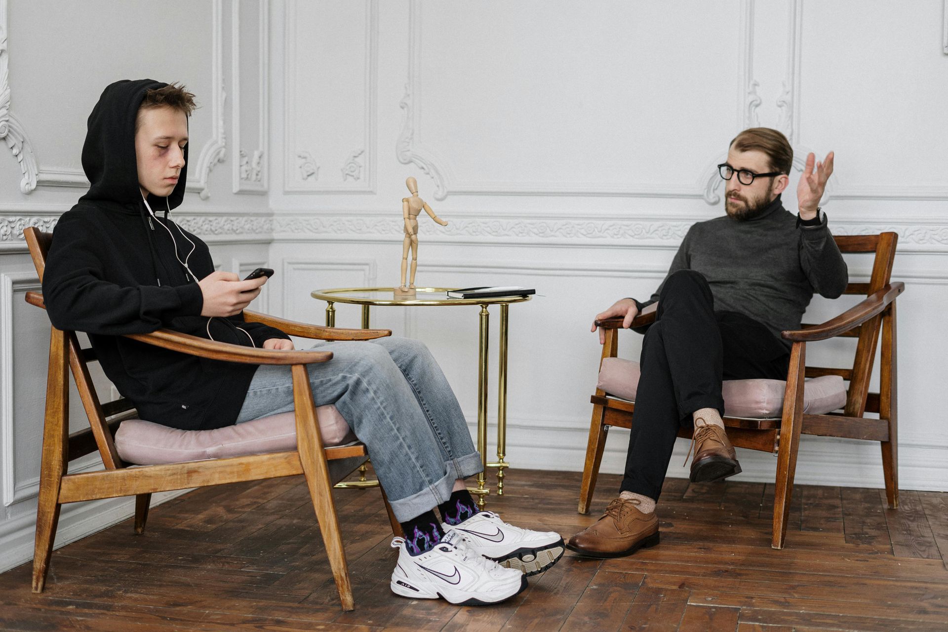 Two men are sitting in chairs talking to each other in a living room.