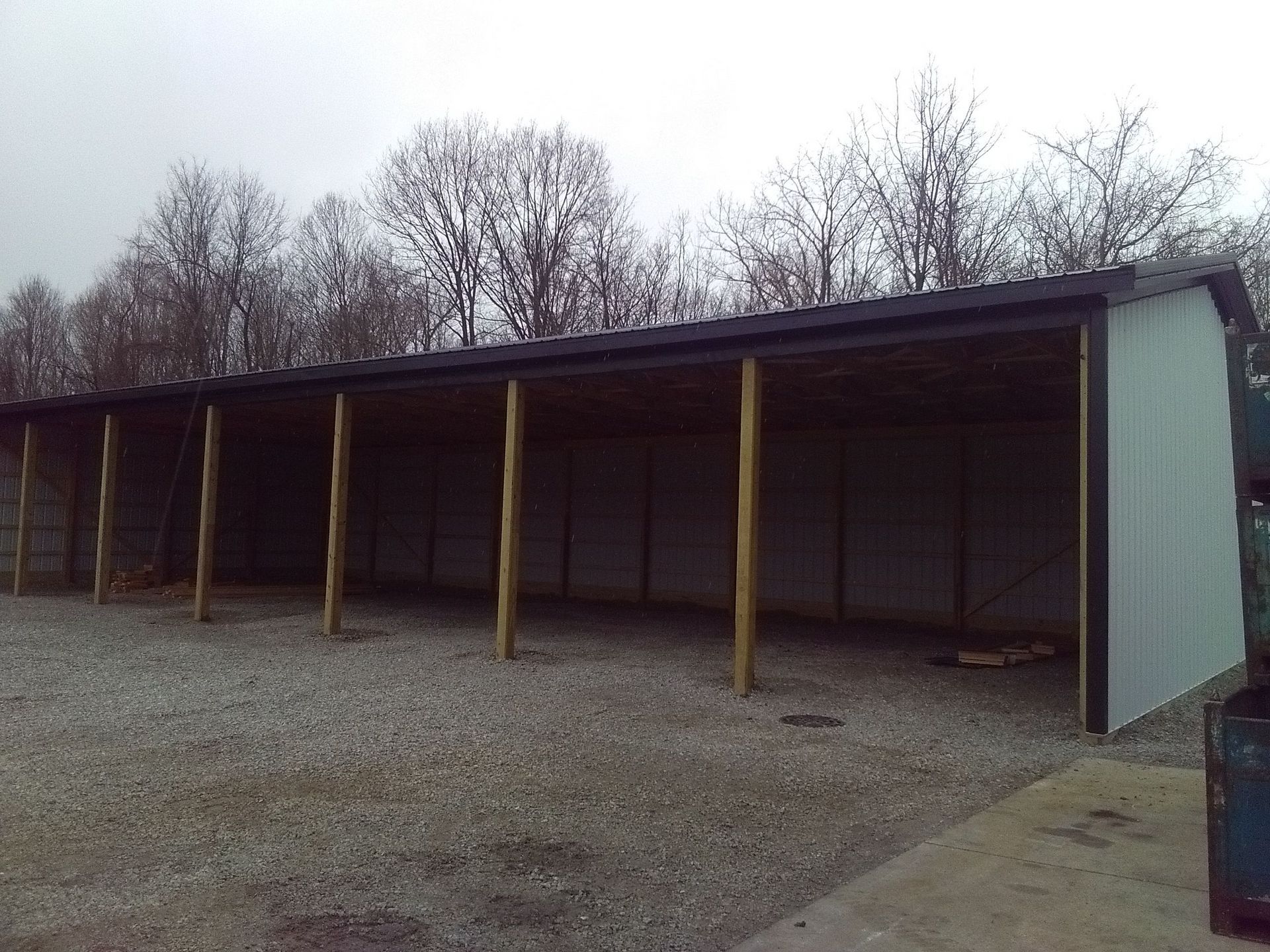 A row of sheds in a gravel area with trees in the background.