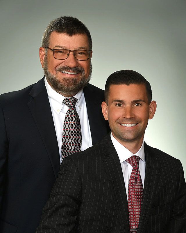 Two men in suits, smiling, posing in front of a neutral backdrop.