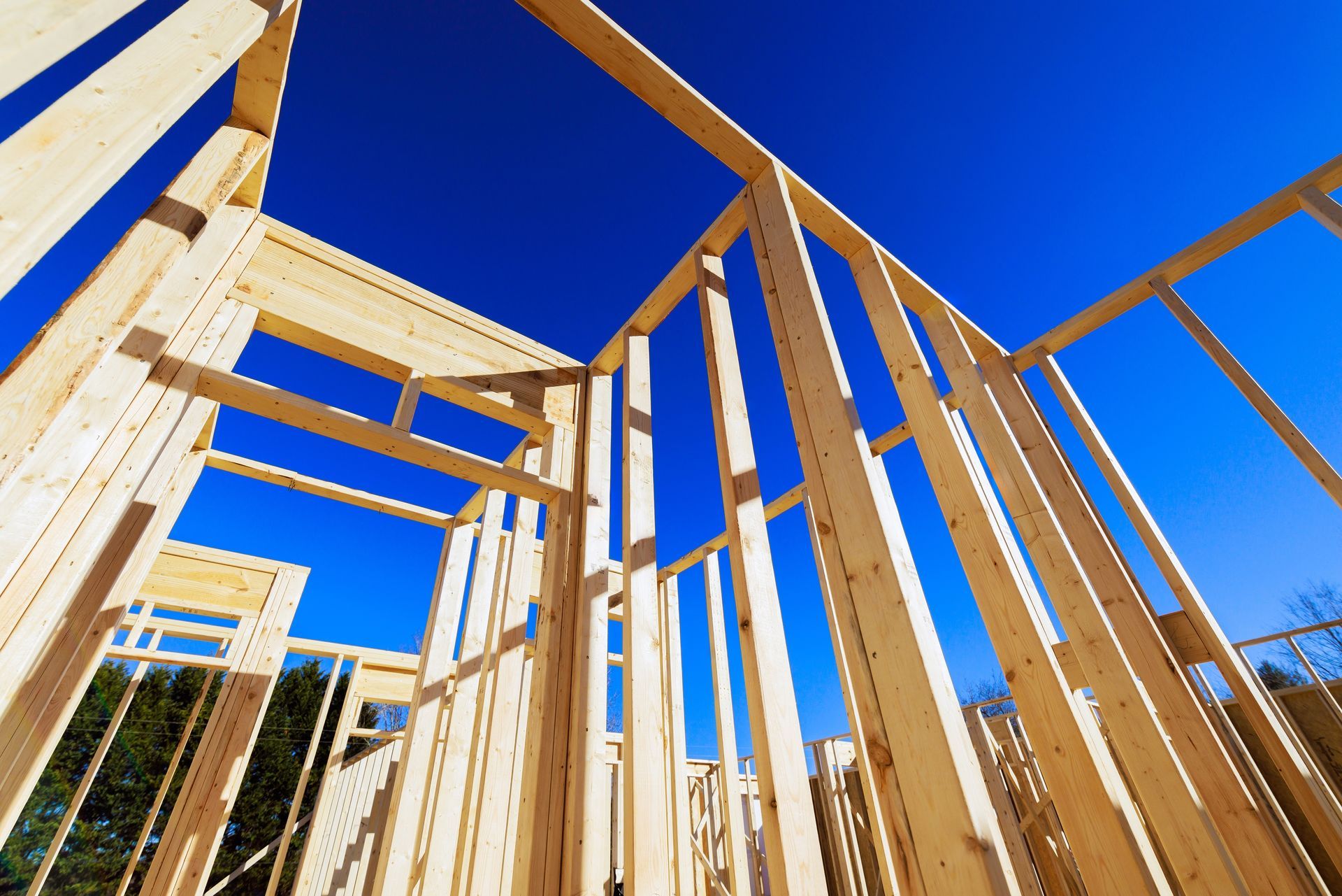 The wooden frame of a building under construction against a clear blue sky.