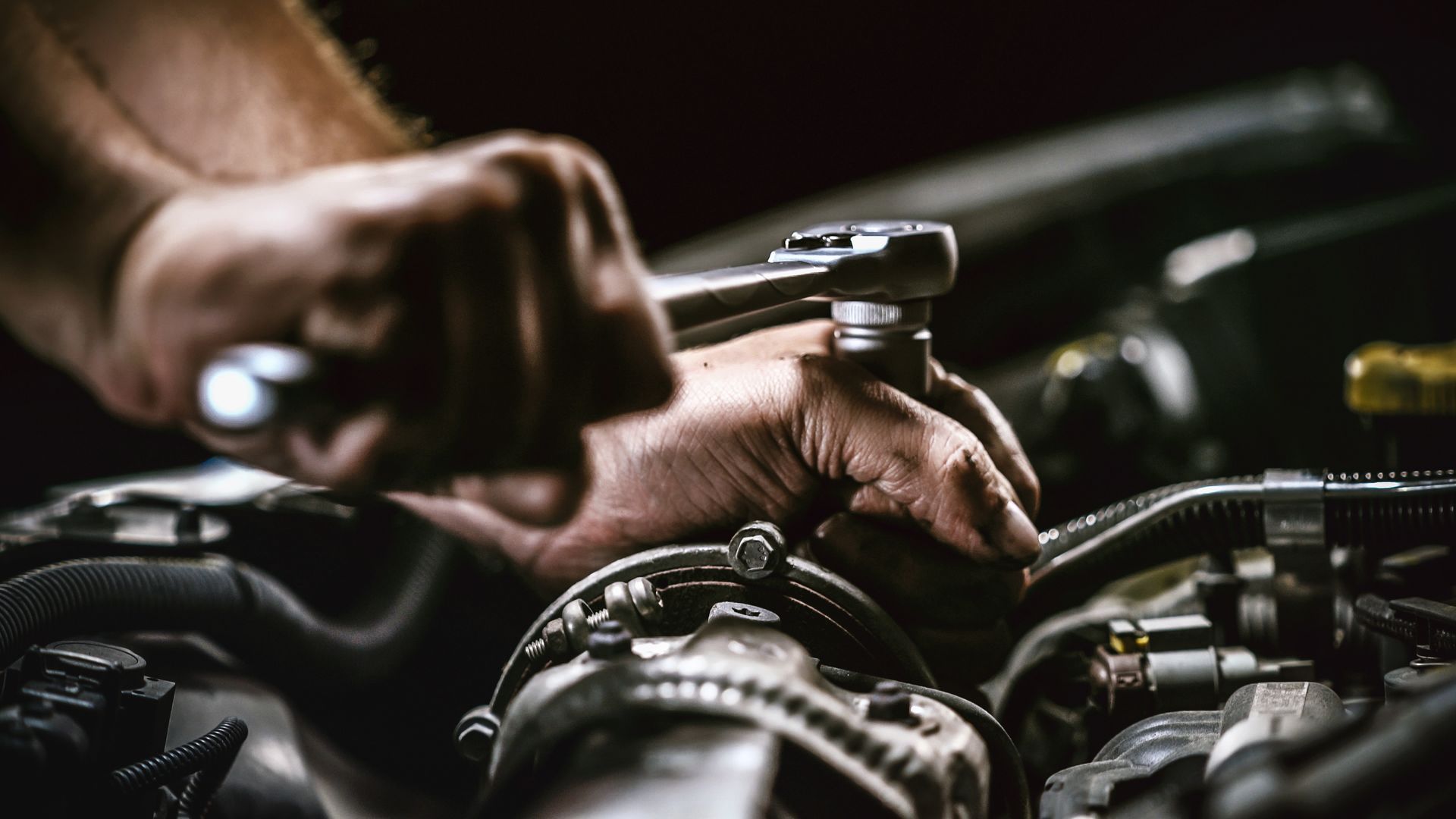 A man is working on a car engine with a wrench.| Bulldog Auto