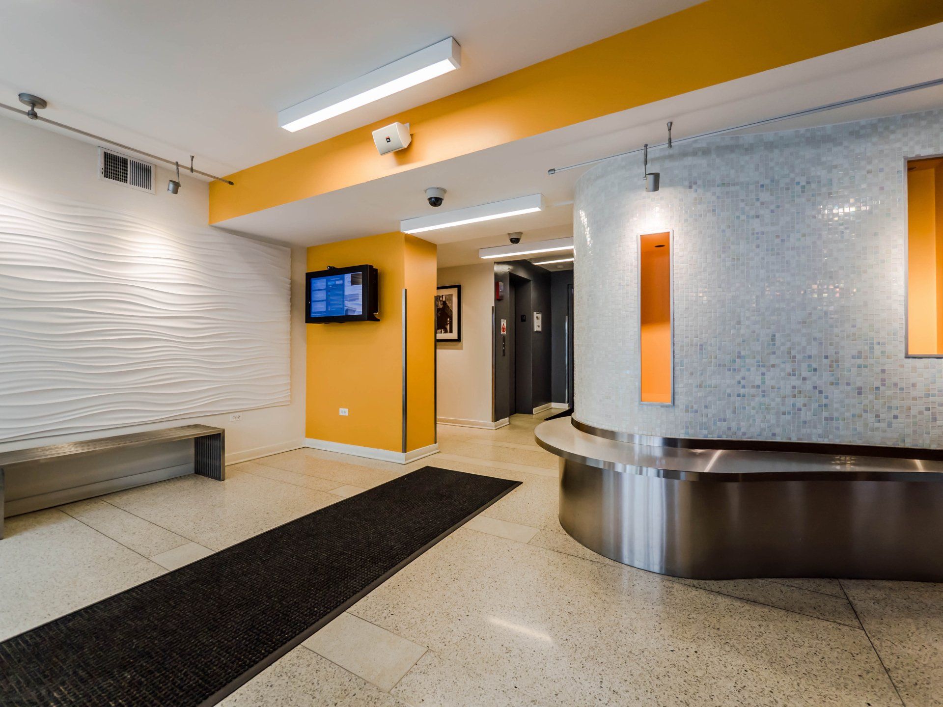 A lobby with a bench and a tv on the wall at Reside on Morse.