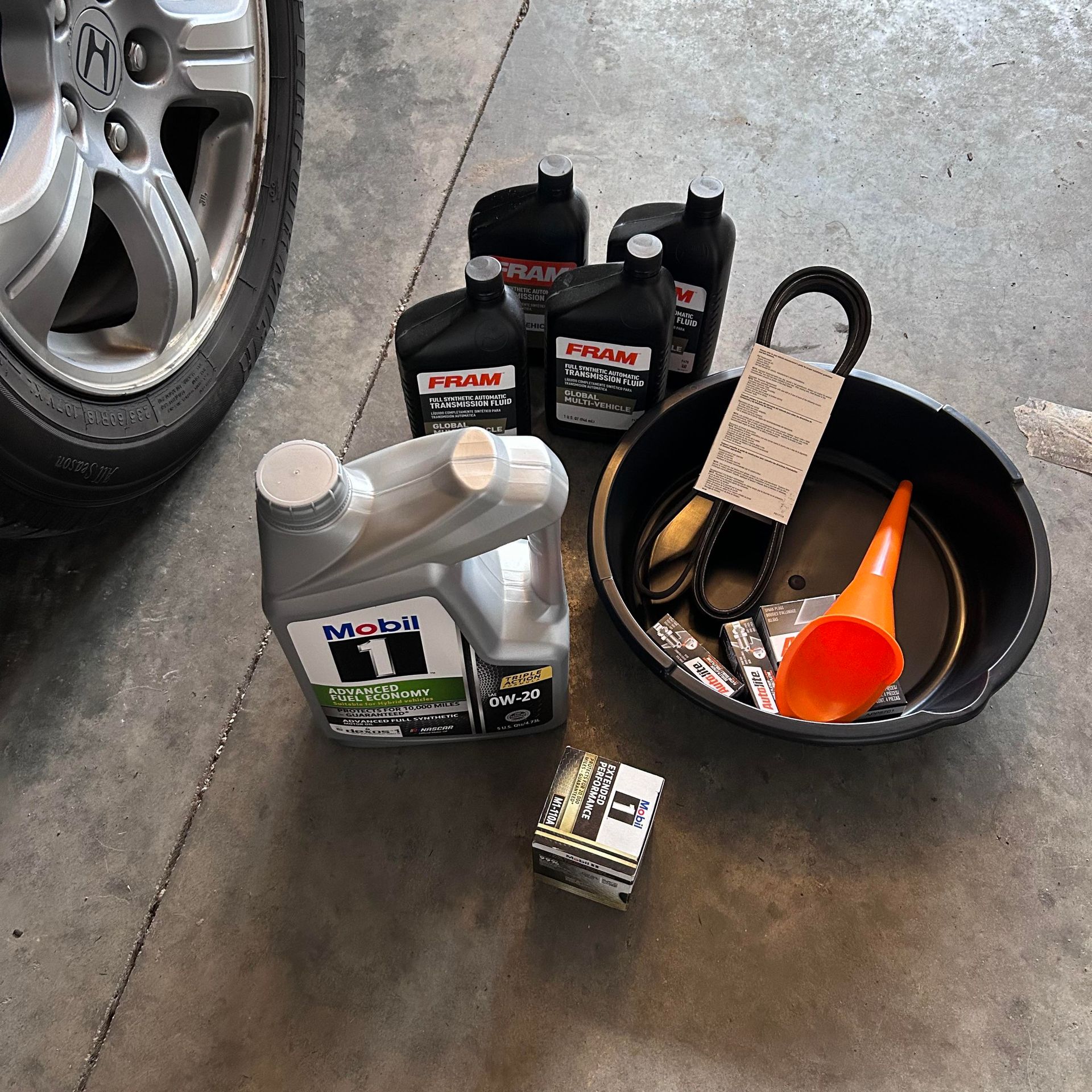 Car oil change supplies: oil bottles, oil filter, drain pan, funnel, and car tire.