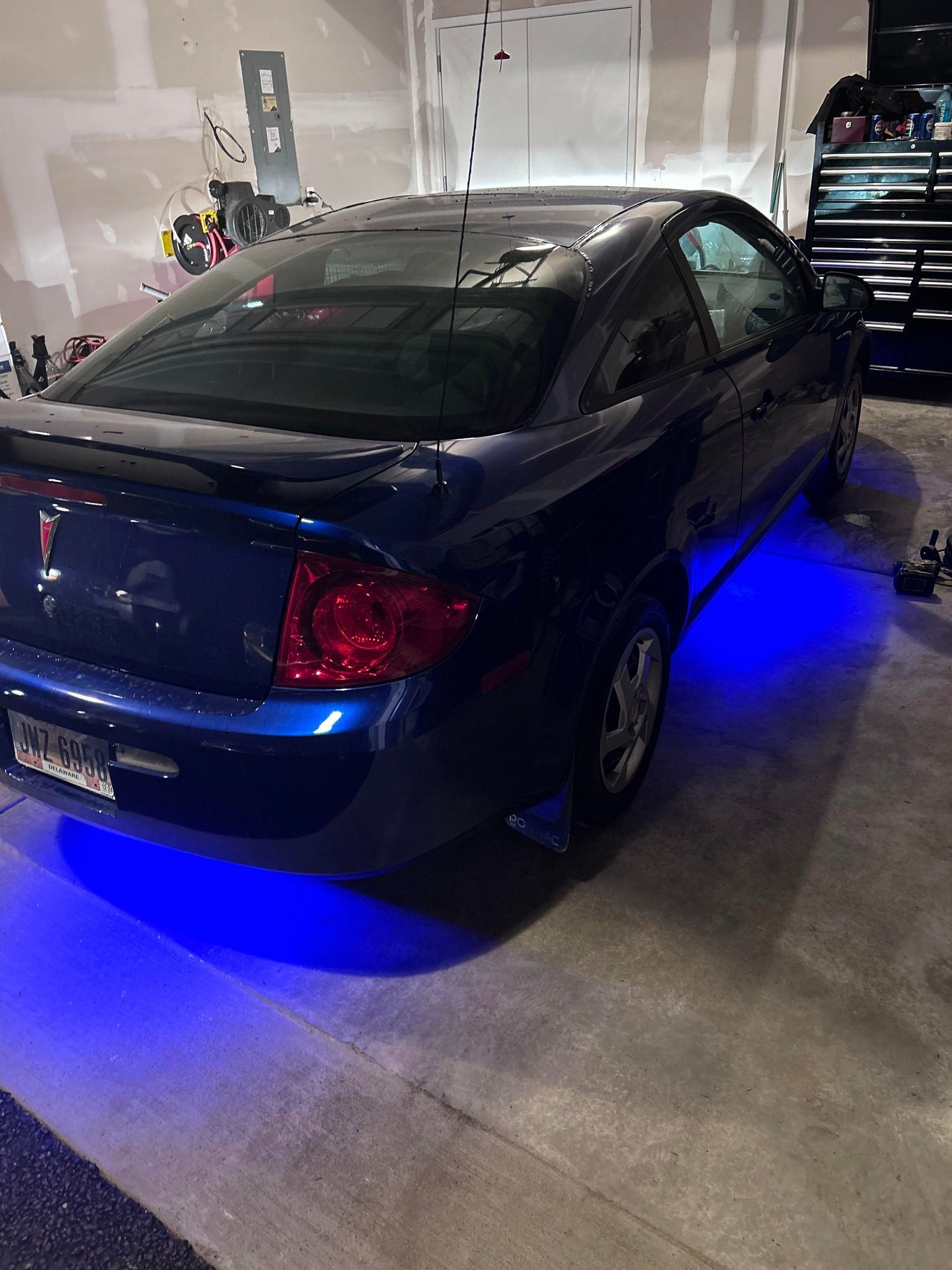 Dark blue car in a garage with blue underglow lights. Tail lights are red. Garage door is in the background.