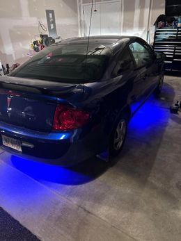 Dark blue car in a garage with blue underglow lights. Tail lights are red. Garage door is in the background.