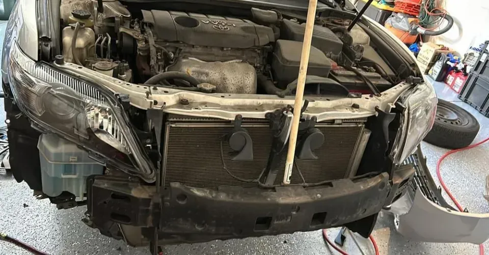 Car with front bumper removed, revealing engine components and radiator.
