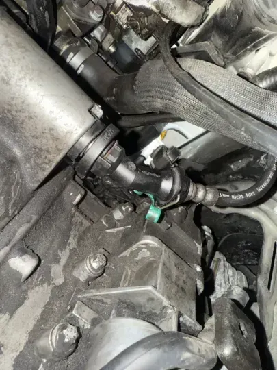 Engine compartment detail with black plastic connectors and hoses, green release clip visible.